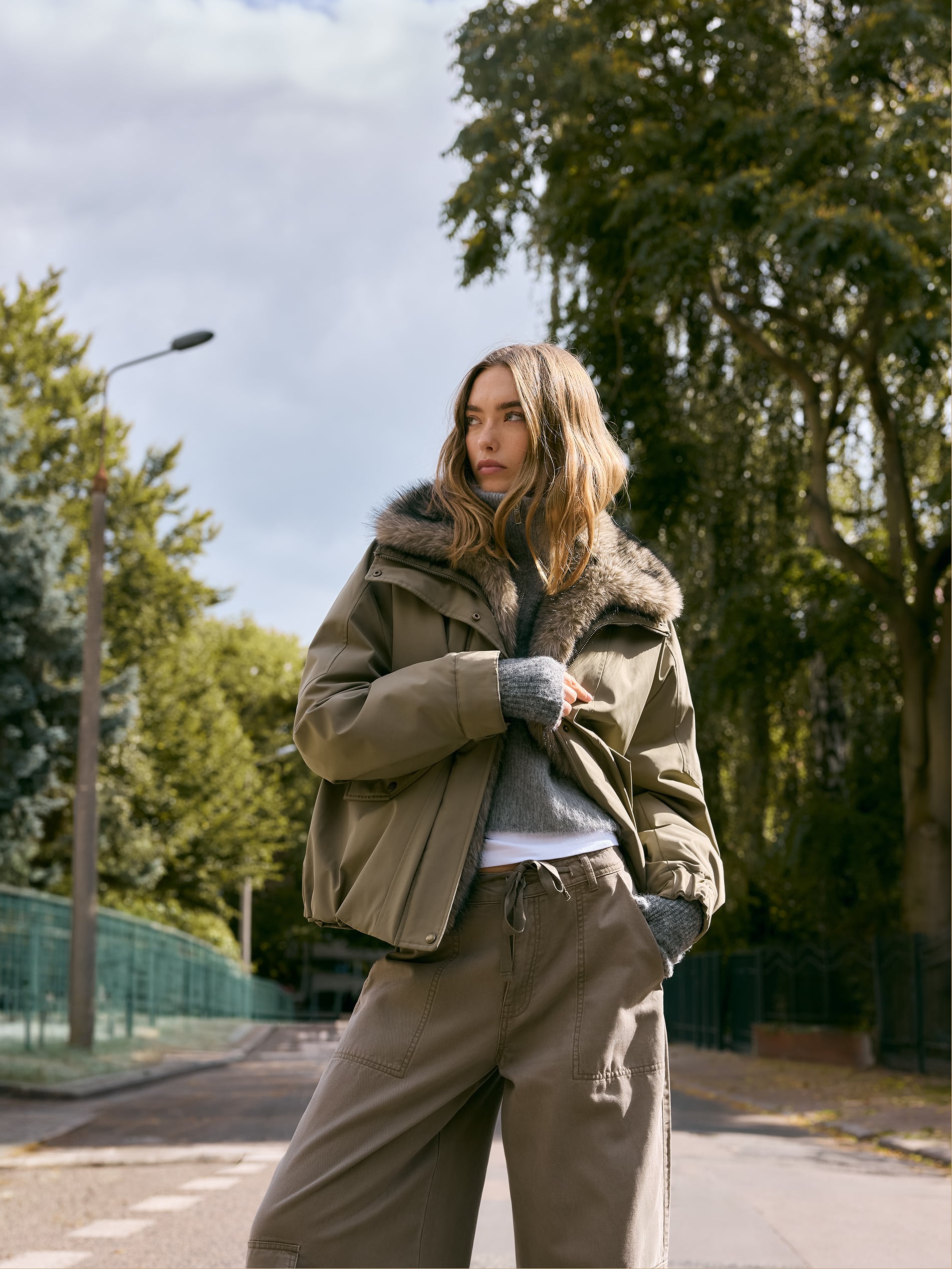 Jachetă utilitară kaki, purtată peste un pulover gri și pantaloni largi în tonuri naturale. Gulerul din blană artificială oferă volum și transformă piesa practică într-un element central al ținutei. (Sursa foto: Reserved)