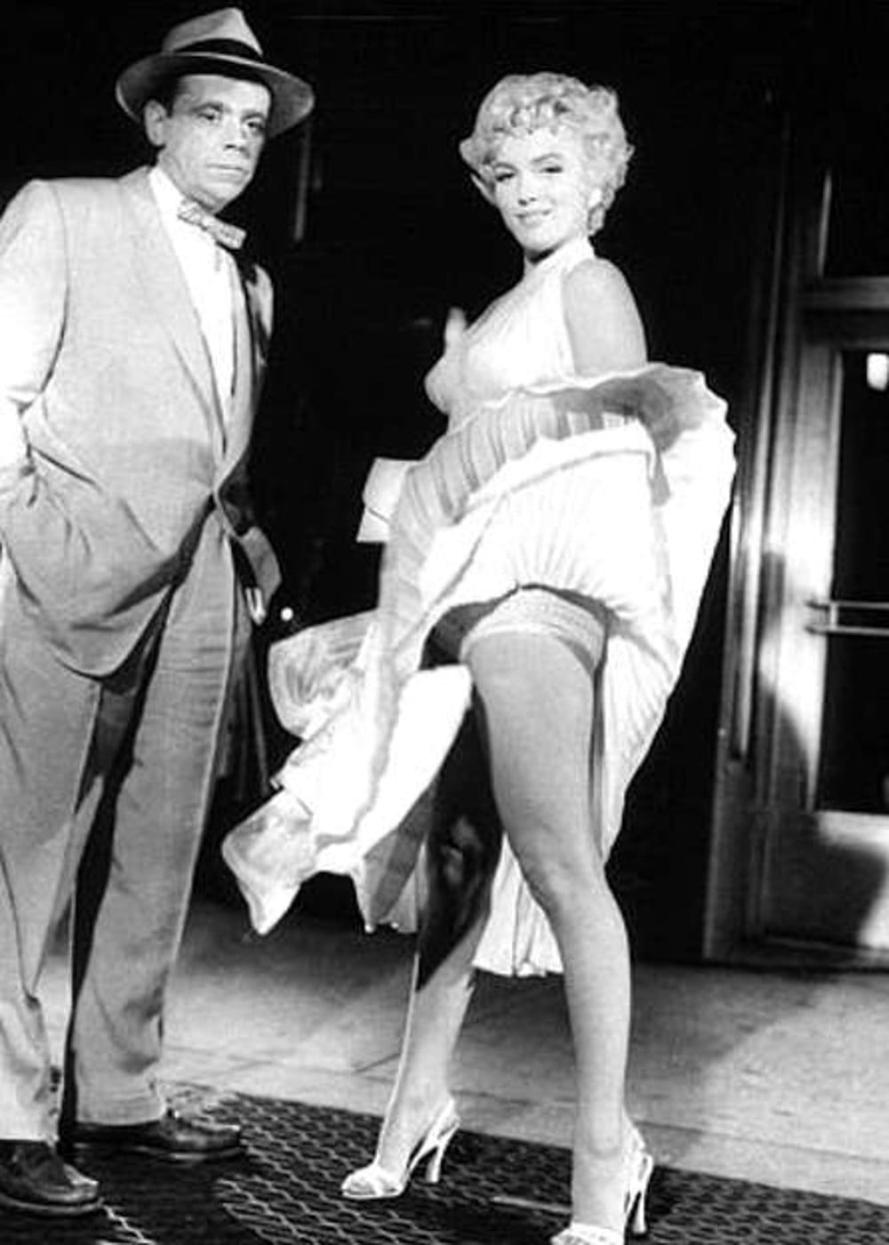 Marilyn Monroe și Tom Ewell într-o scenă din comedia romantică „The Seven Year Itch” (1955), regizată de Billy Wilder. Filmul urmărește povestea lui Richard Sherman, un bărbat căsătorit care rămâne singur în New York pe timpul verii. (Sursa foto: Profimedia)